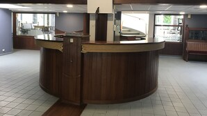 A circular wooden reception desk with a woven counter, a white pillar, and a view of a staircase leading to a balcony. - Le Salin (Brehal)