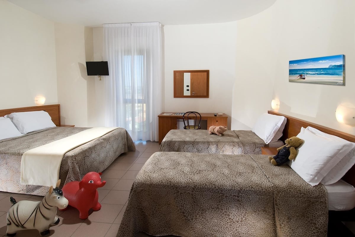 Une chambre d’hôtel avec deux lits, un bureau, une chaise, une télévision, un miroir et un tableau représentant une plage.