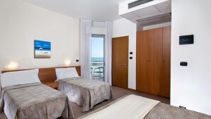 Een hotelkamer met twee bedden, een groot raam met uitzicht, een deur en een luchtventilator in het plafond.