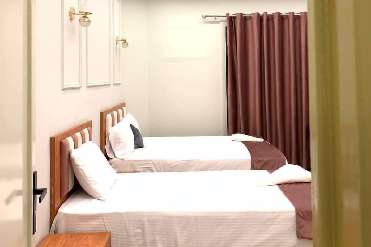 Ein Hotelzimmer mit zwei Betten, einem hölzernen Nachttisch, einer Wandlampe und einem Vorhang.