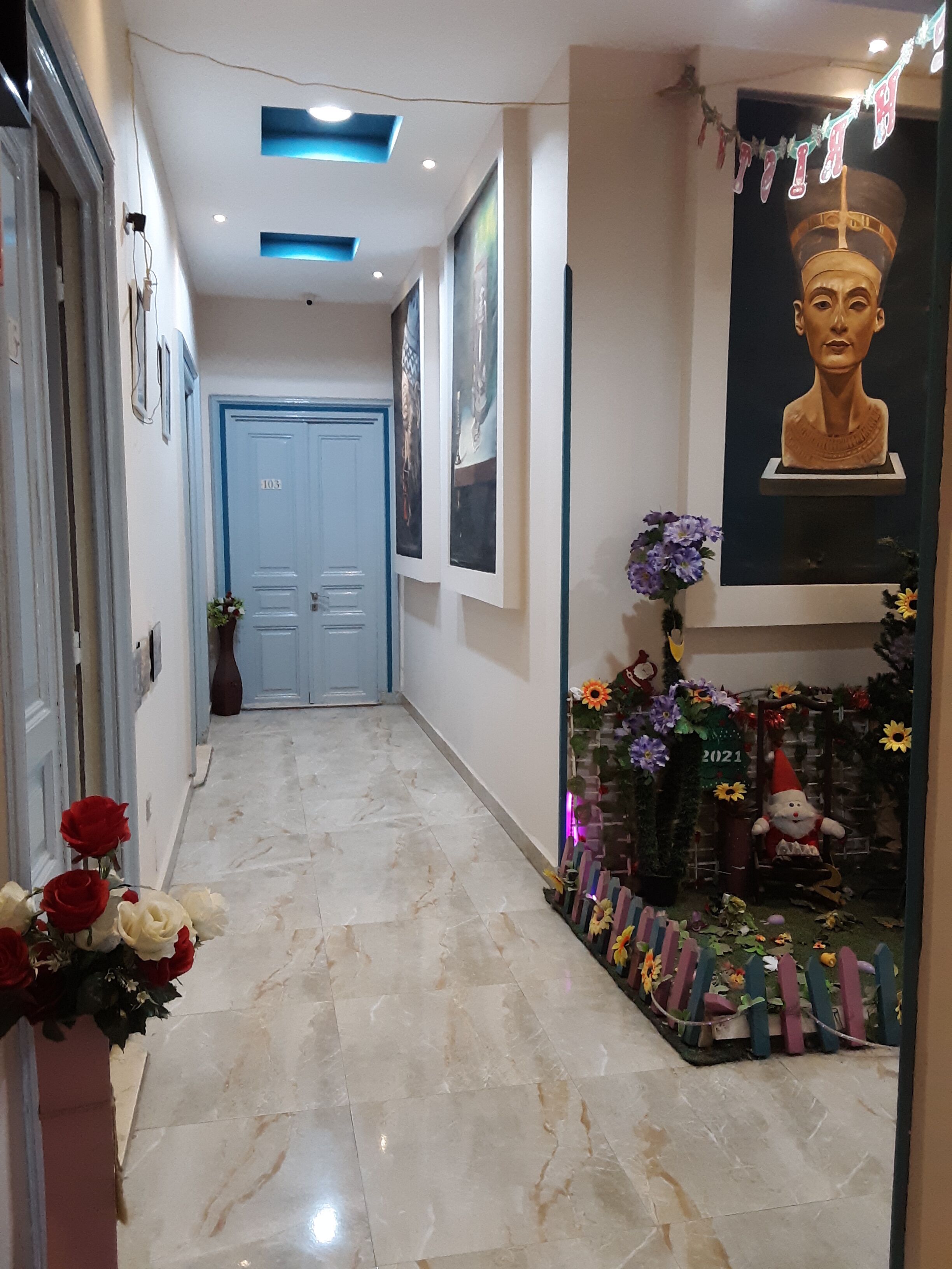 A hallway with a marble floor, a blue door, and a decorative area with flowers and a gnome statue.