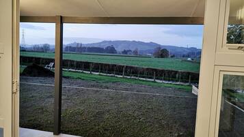 A view from a room with a large window overlooking a rural landscape with fields, a fence, and distant hills.