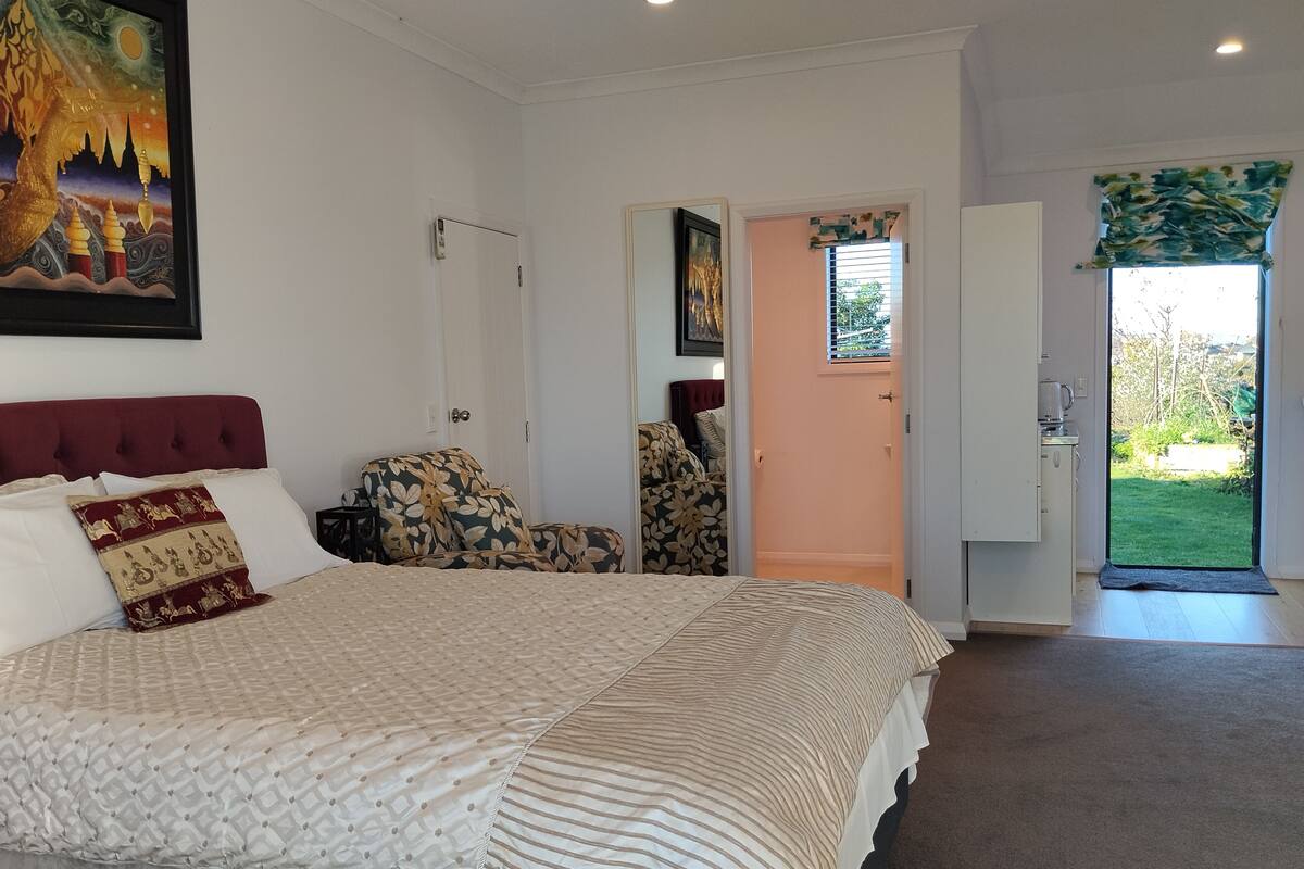 A bedroom with a bed, a chair, a door leading to a balcony, and a painting on the wall.