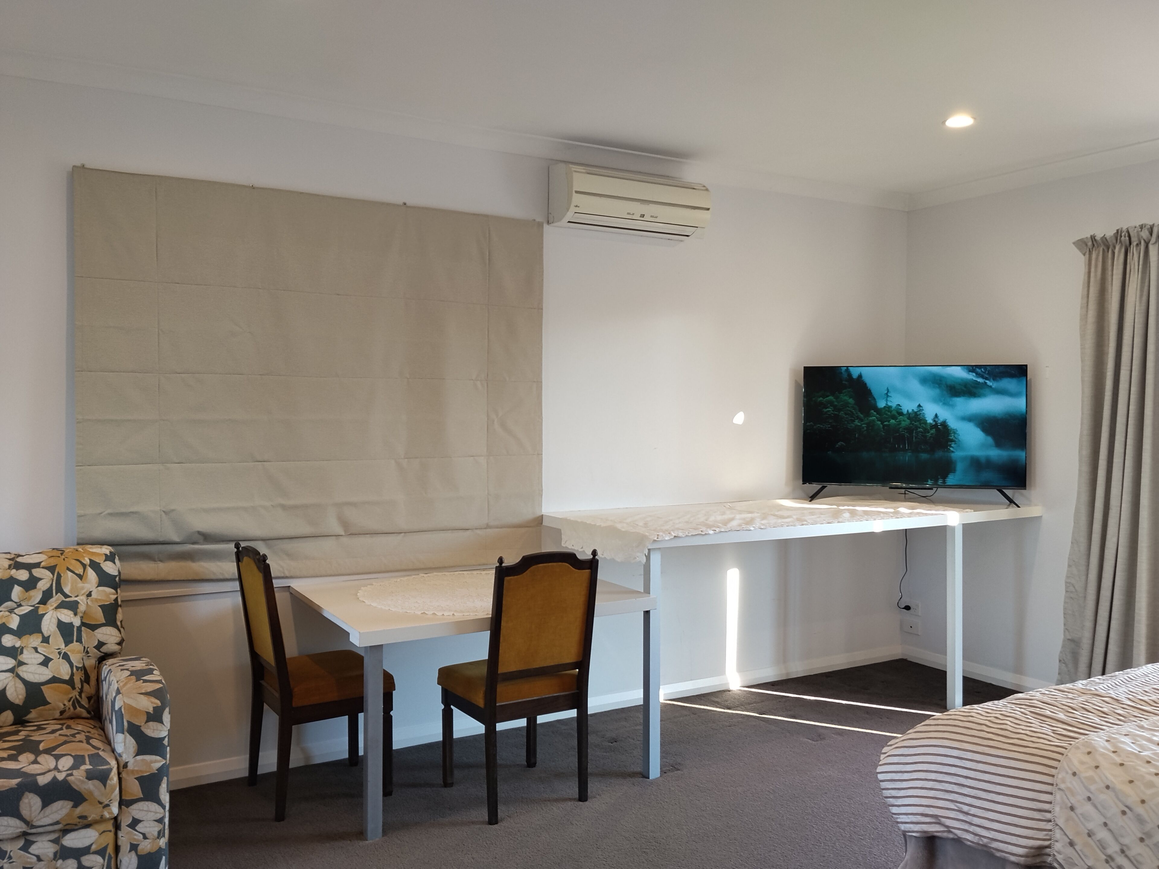 A room with a bed, a desk with two chairs, a TV, and an air conditioner.
