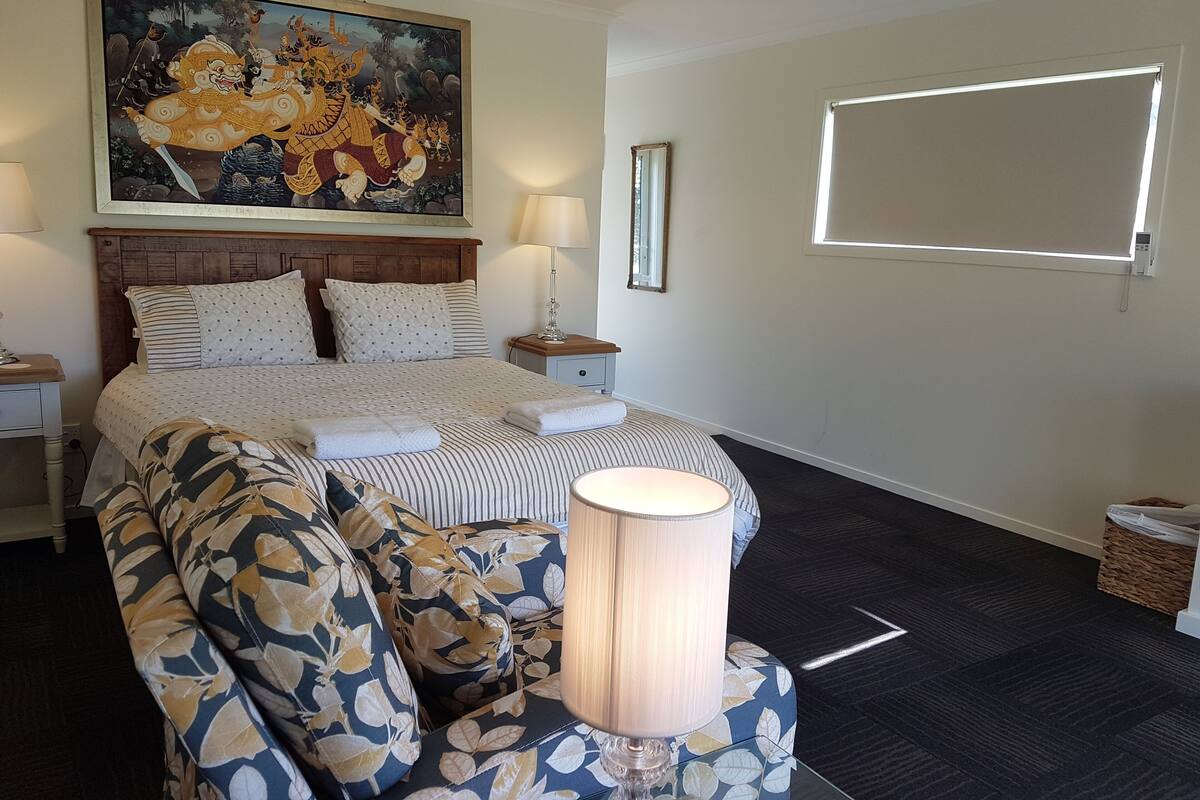 A hotel room with a large bed, a headboard, a nightstand, a lamp, a painting, and a window.
