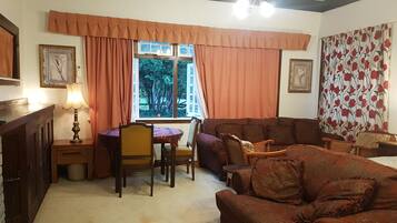 Una sala de estar acogedora con un sofá, sillas, una mesa y un ventanal con cortinas.