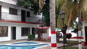 Un edificio a due piani con piscina, palme e un balcone.