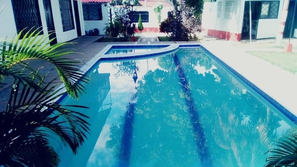 Una piscina con superficie d'acqua cristallina e blu, circondata da un solarium in cemento e palme.