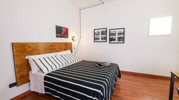 Une chambre à coucher avec une tête de lit en bois, une couvre-lit à rayures noires et blanches, une table de chevet avec une lampe, et deux tableaux encadrés accrochés au mur.