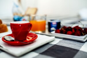 Un desayuno con una taza roja, un vaso de zumo de naranja y un plato de cerezas.