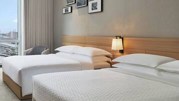 Habitación de hotel con dos camas, una silla, vistas a la ciudad y cuadros en la pared.