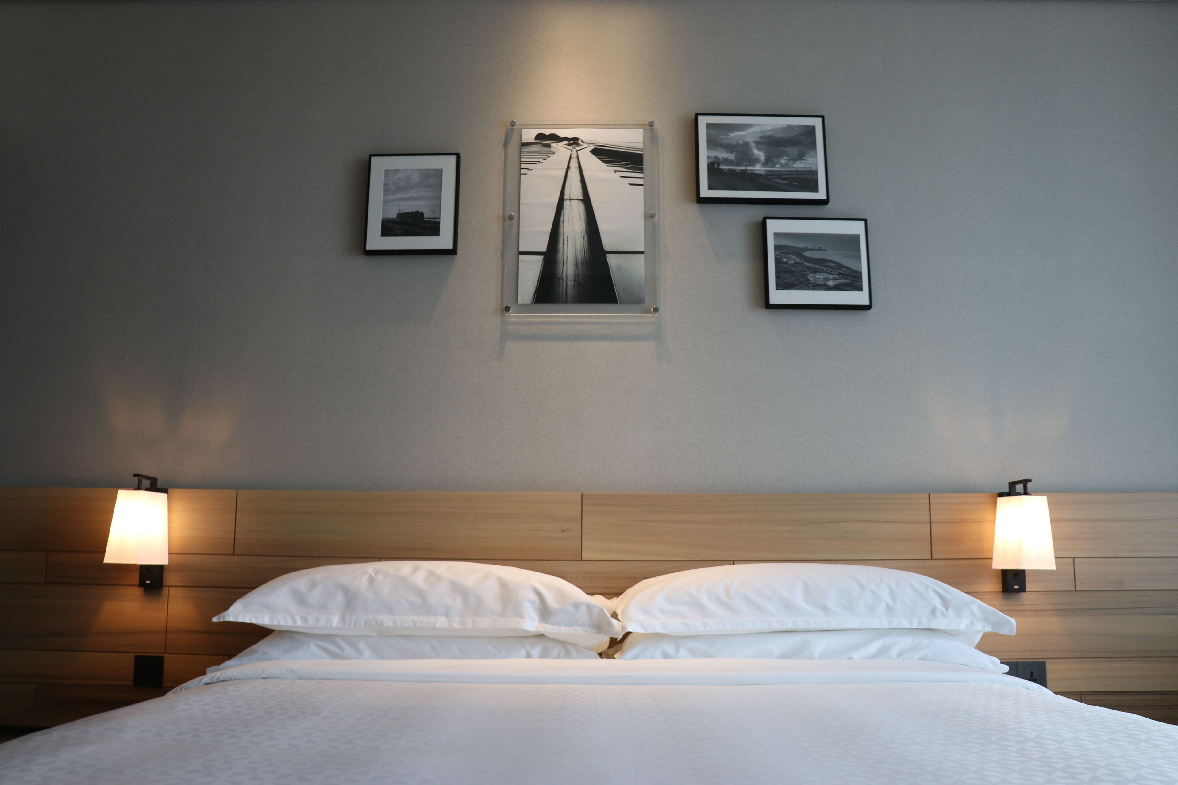 Una habitación de hotel con una cama, dos lámparas fijadas a la pared y tres cuadros enmarcados.