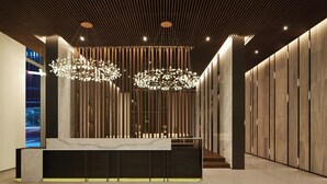 Una moderna zona de recepción con mostrador de mármol, listones de madera en el techo e iluminación colgante.