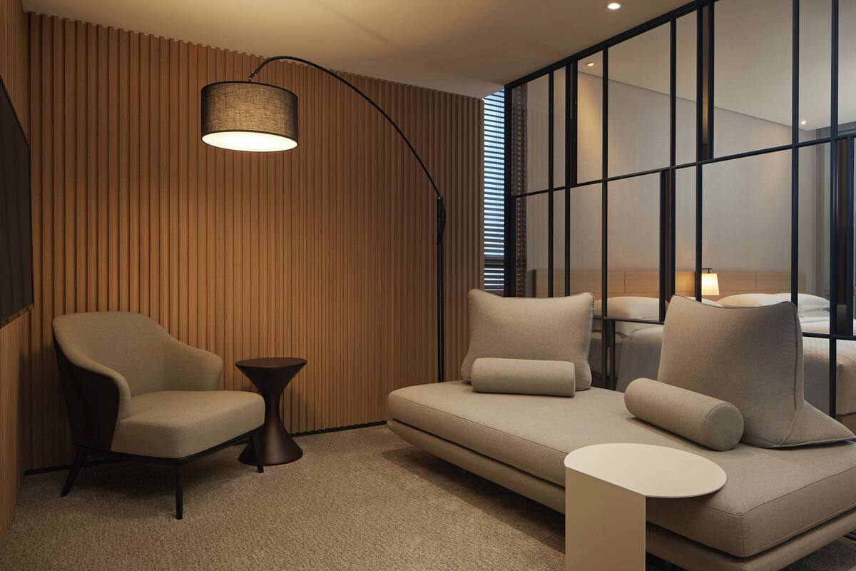 Een moderne woonkamer met een bank, fauteuils, een klein bijzettafeltje en een vloerlamp.