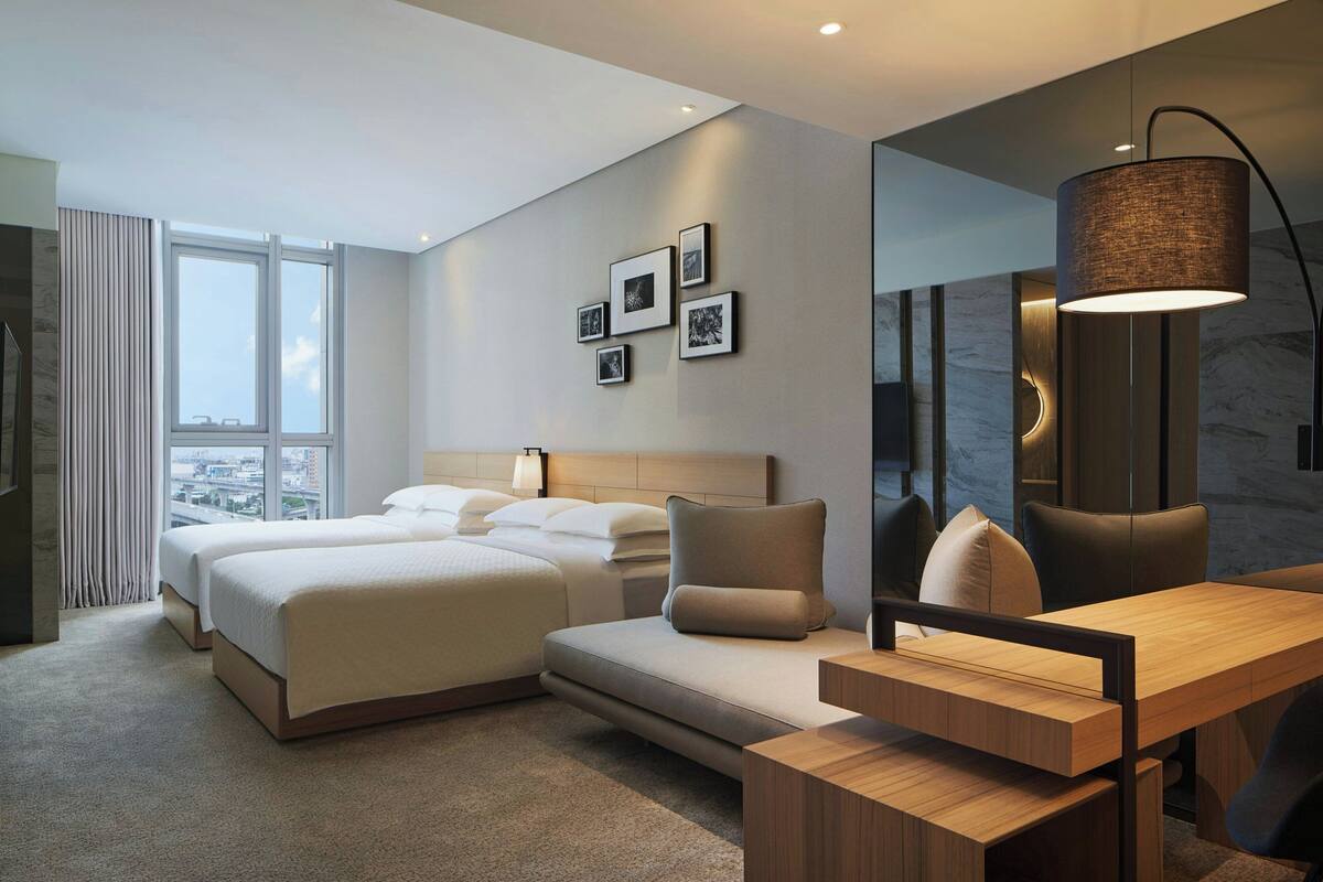 Een moderne hotelkamer met een groot bed, een sofa, een bureau en uitzicht over de stad.
