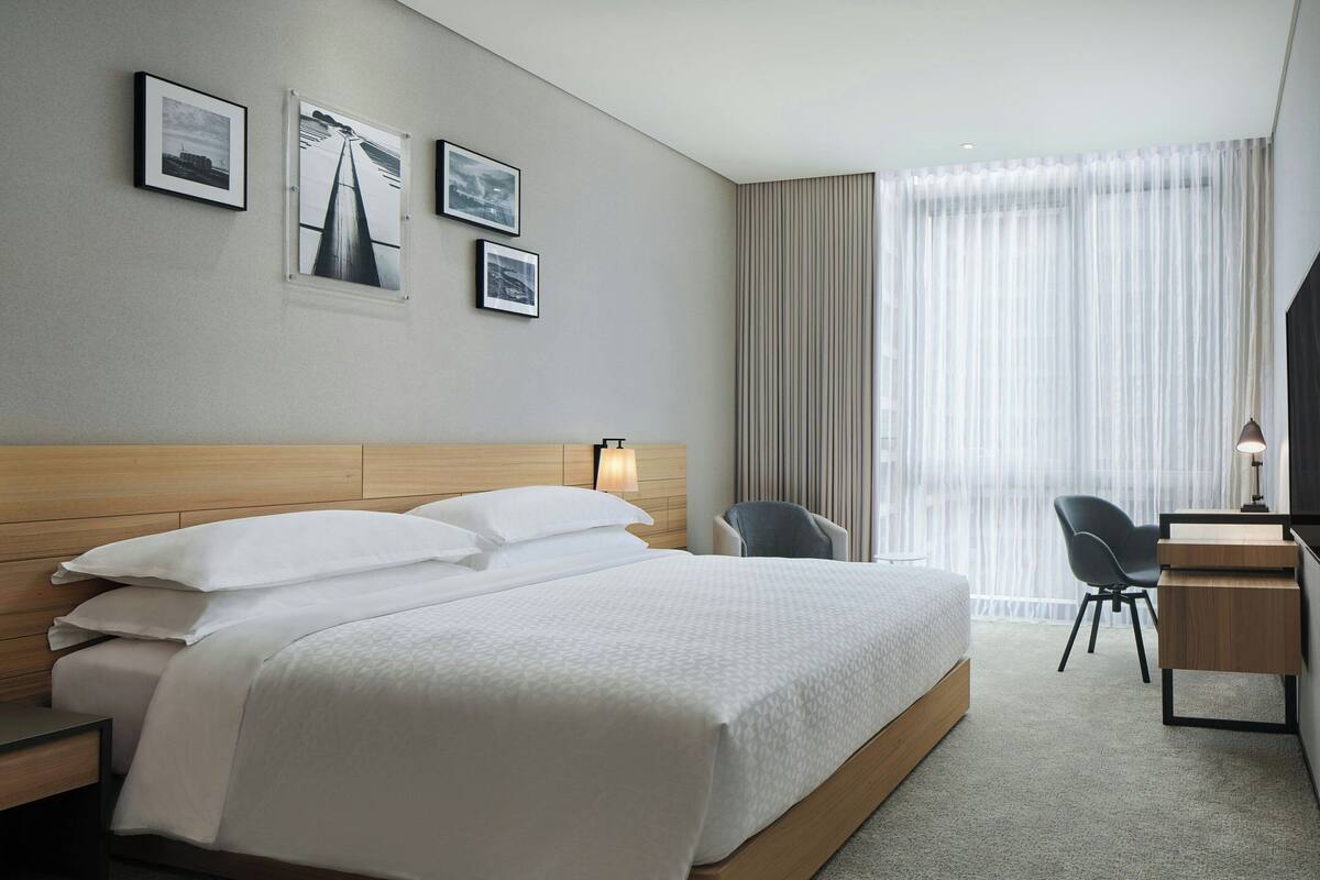 Een hotelkamer met een groot bed, een bureau en een stoel. Drie ingelijste foto's hangen aan de muur.