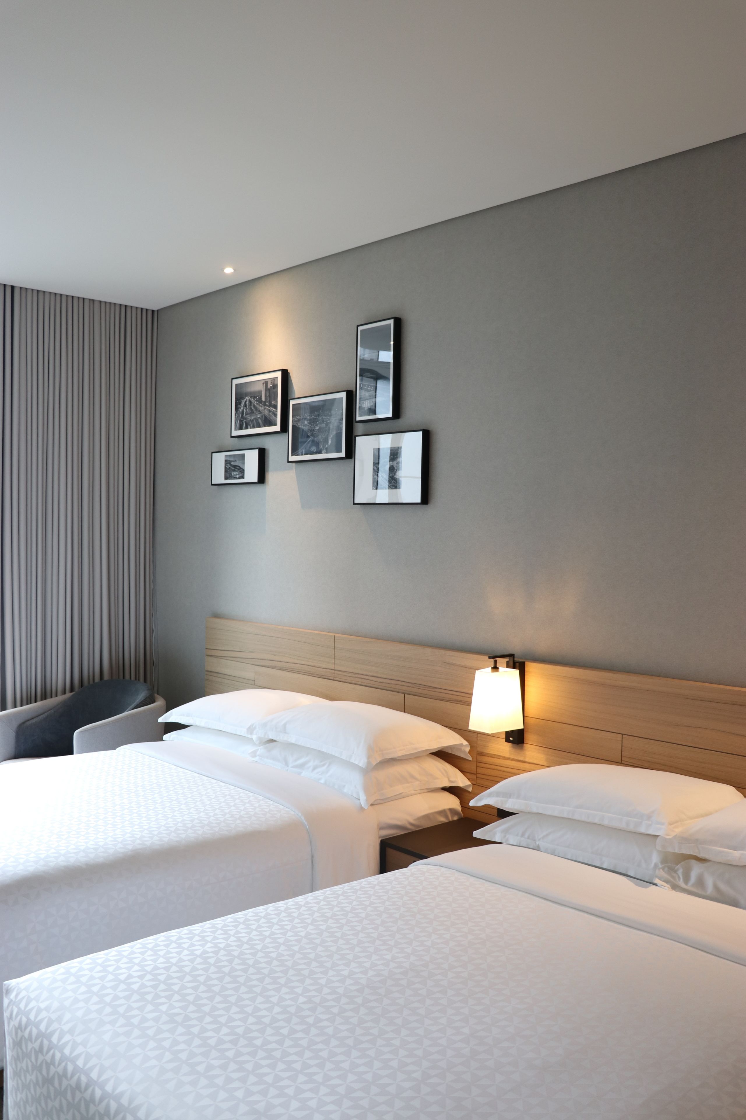 Una habitación de hotel con dos camas, cabeceros, una lámpara de pared y cuadros enmarcados.