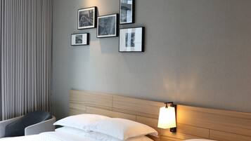 Una habitación de hotel con dos camas, cabeceros, una lámpara de pared y cuadros enmarcados.