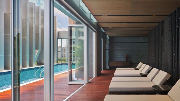 Un área de piscina interior moderna con paredes de vidrio, suelo de madera y sillones de descanso.