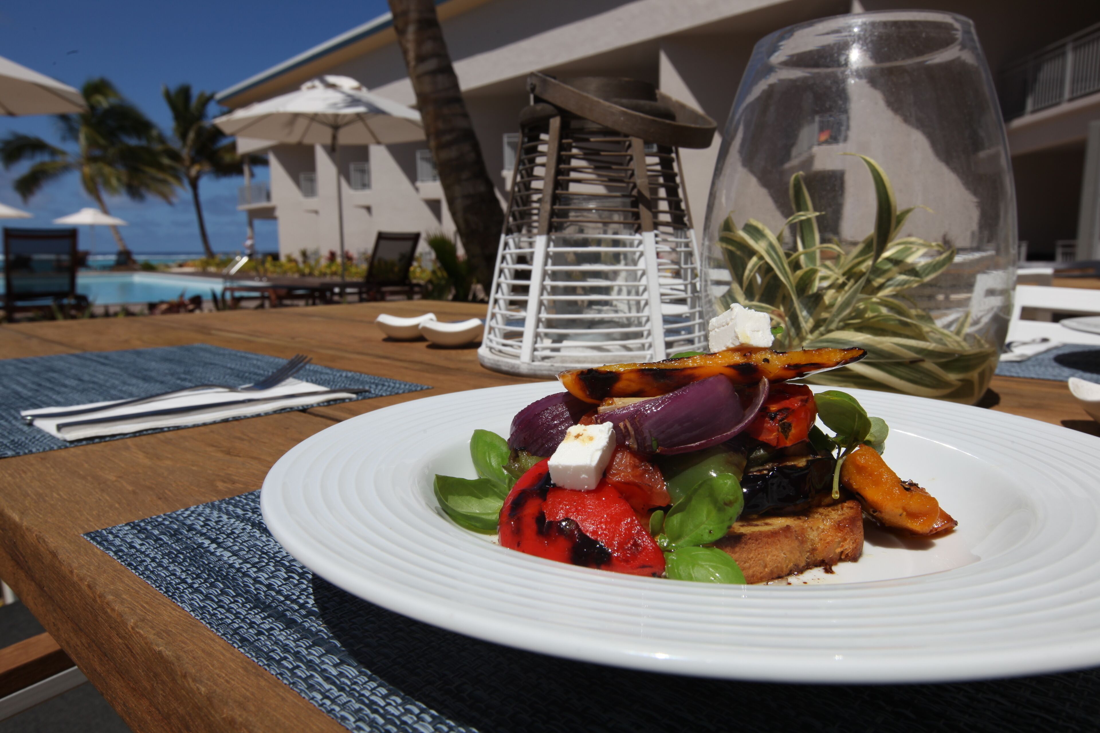 A dining table with a plate of grilled vegetables and feta cheese, a glass of water, and a decorative lantern.
