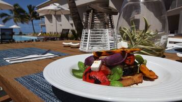 A dining table with a plate of grilled vegetables and feta cheese, a glass of water, and a decorative lantern.