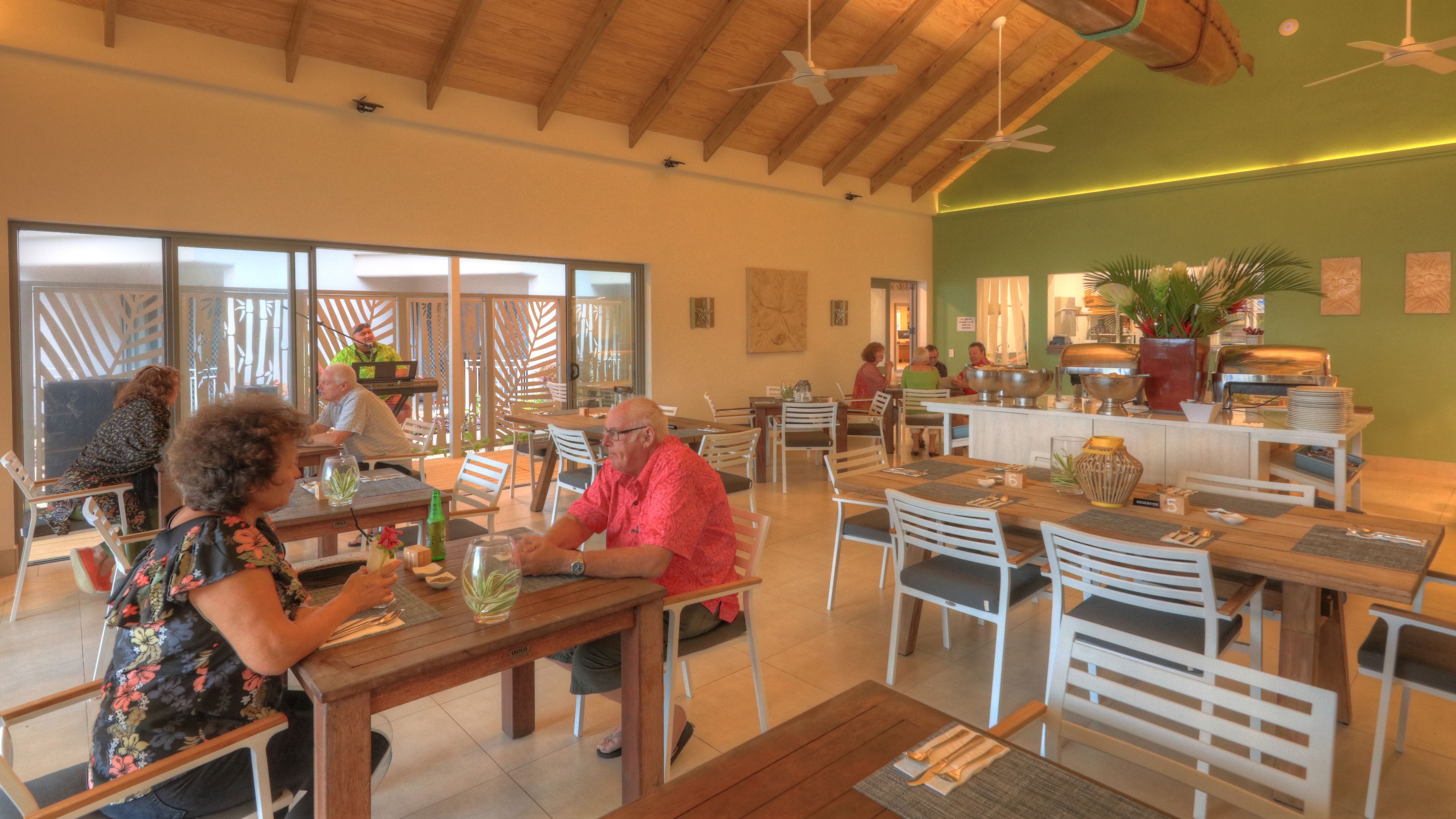 A restaurant with wooden tables and chairs, a buffet area, and a green wall with artwork.