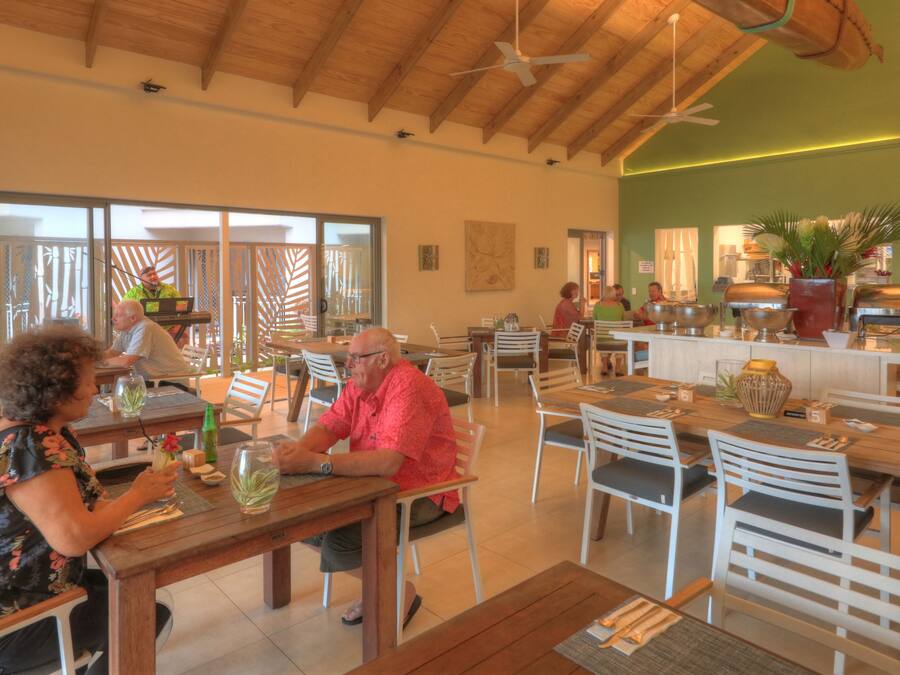 A restaurant with wooden tables and chairs, a buffet area, and a green wall with artwork.