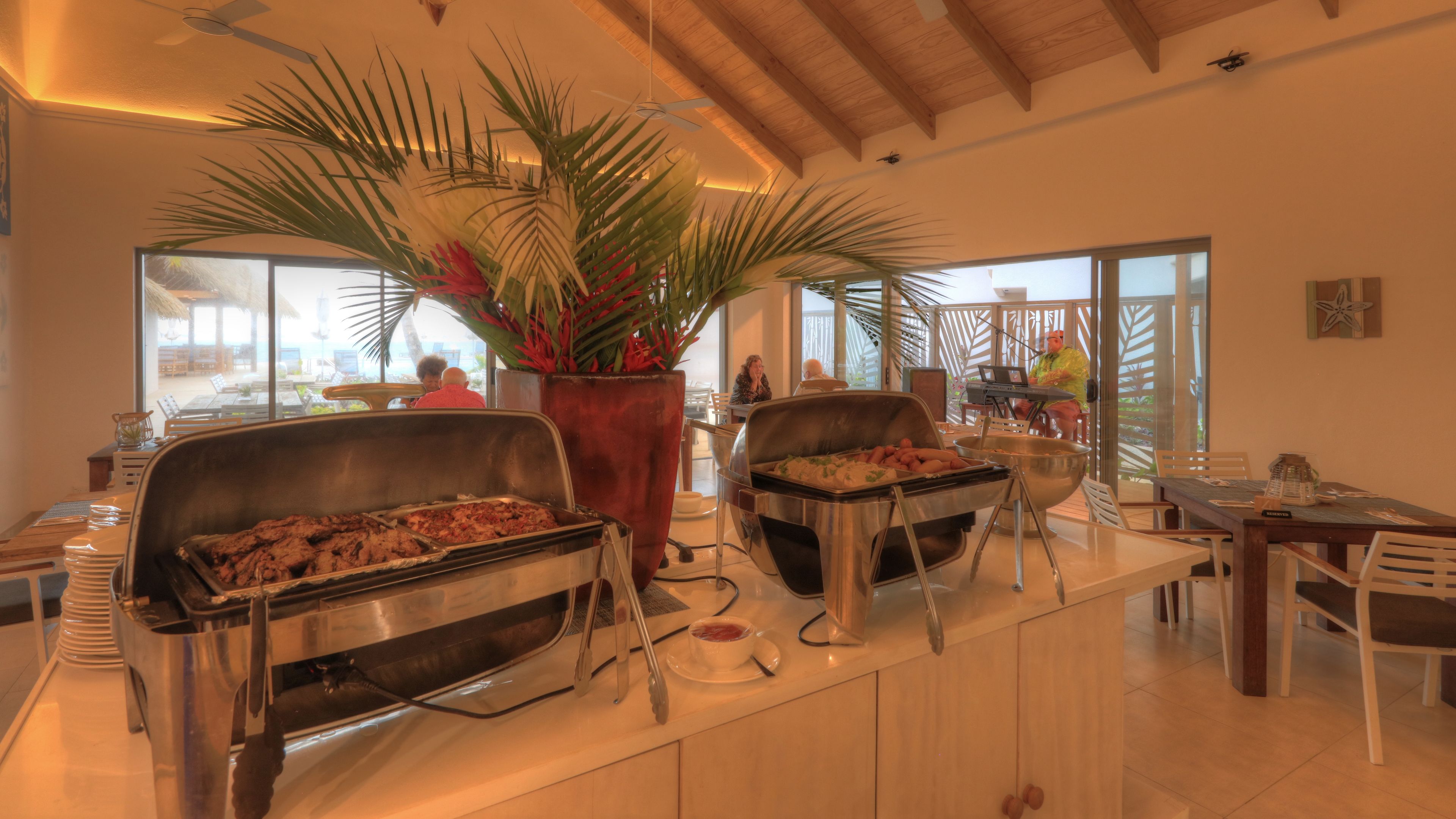 Un comedor moderno con dos parrillas, una planta grande en maceta y vistas del espacio exterior con mesas.