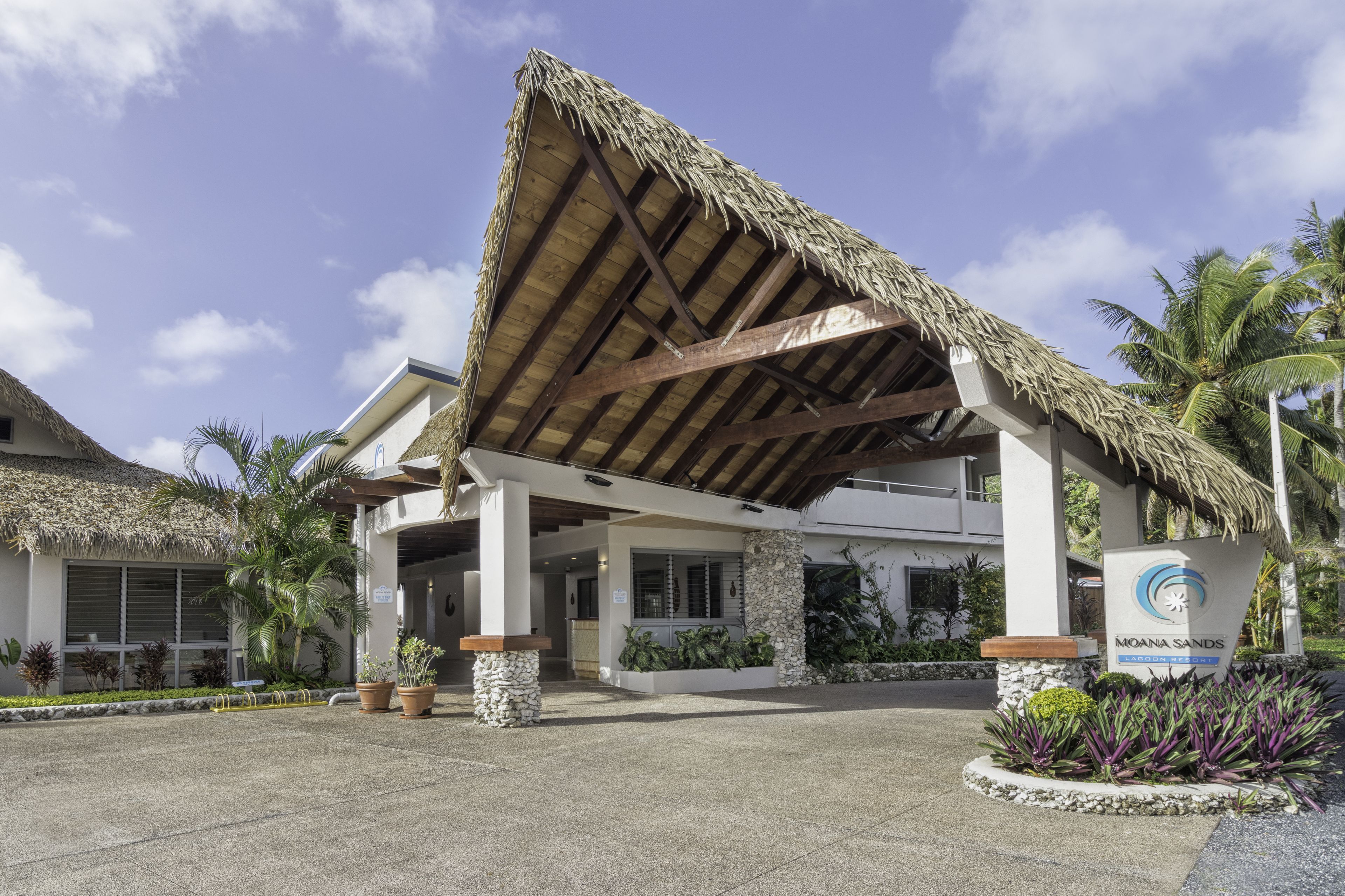A resort entrance with a thatched roof, palm trees, and a sign for Moana Sands.