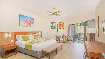 Habitación de hotel con cama, escritorio, silla, banco, ventilador de techo y obras de arte en las paredes.