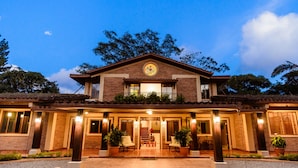 A two-story house with a tiled roof, a front porch with seating, and a circular emblem above the entrance. - Caracoral Hotel Boutique & Spa (El Valle de Anton)