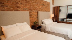 A hotel room with two beds, a brick wall, a wooden cabinet with a television, and a small table with a lamp. - Caracoral Hotel Boutique & Spa (El Valle de Anton)