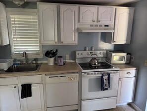 Una cocina con armarios blancos, estufa, microondas y fregadero.
