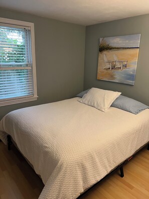 A bedroom with a bed, a window with blinds, and a beach-themed painting on the wall. - Walk to the Beach!!! (Centerville)