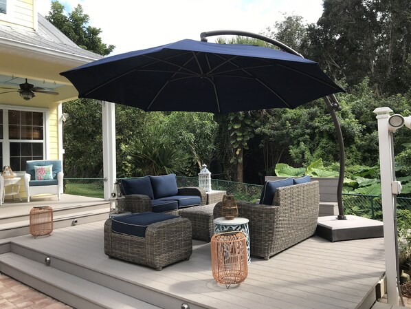 A covered outdoor deck with wicker furniture, a large umbrella, and a lantern.