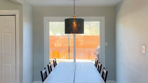 Een eetkamer met een lange tafel en stoelen, een hangende lamp en uitzicht op een achtertuin.