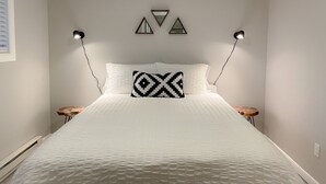 Een net opgemaakt bed met een gestreept kussen, twee nachtkastjes en wandlampen.