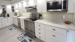 A modern kitchen with white cabinetry, stainless steel appliances, and a marble countertop. - The Shore 211-Stylish 2BR Gulffront Condo with Stunning Sunsets & Pool by RVA (Longboat Key)