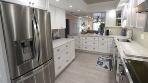 A modern kitchen with stainless steel appliances, white cabinetry, and a central island. - The Shore 211-Stylish 2BR Gulffront Condo with Stunning Sunsets & Pool by RVA (Longboat Key)