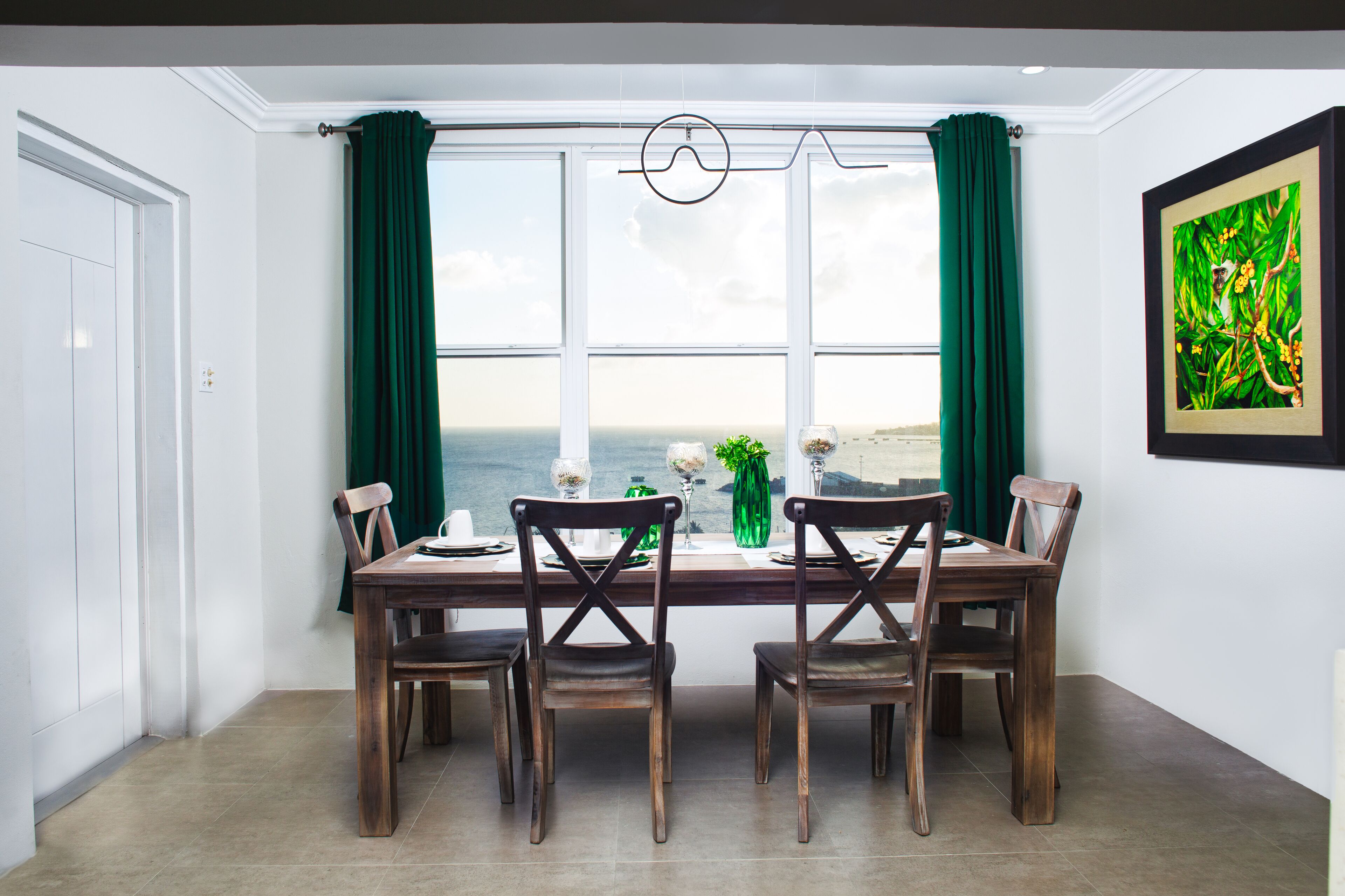 Un comedor con vistas al océano, una mesa de madera y cortinas verdes.