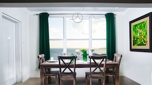 Un coin repas avec vue sur l’océan, une table en bois et des rideaux verts.