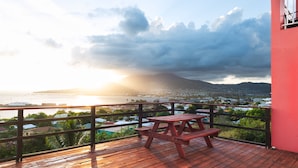 Une terrasse en bois avec une table de pique-nique, offrant une vue sur la côte et une montagne en arrière-plan.