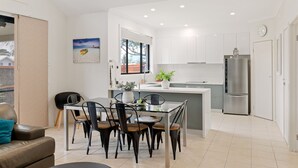 Eine moderne Küche mit weißen Schränken, einem Edelstahlkühlschrank und einem Essbereich mit einem Glastisch und Metallstühlen.