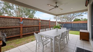 Eine überdachte Terrasse mit einem weißen Tisch und Stühlen, einem Deckenventilator und Blick auf den Garten.