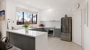 Eine moderne Küche mit weißen Schränken, einem Edelstahlkühlschrank und einem Fenster mit Blick ins Freie.