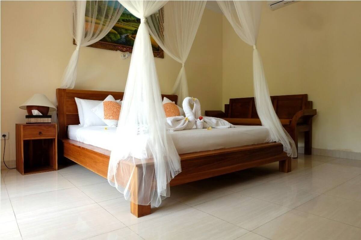 A wooden bed with a canopy, white bedding, and a nightstand with a lamp.