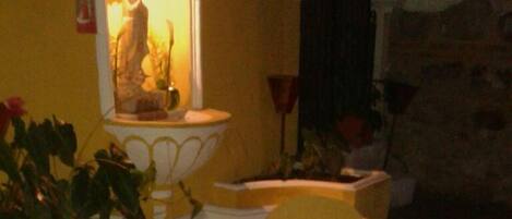 Un comedor con sillas amarillas y una mesa redonda, una estatua al fondo y suelo de baldosas.