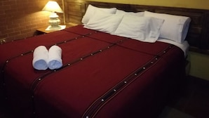 A neatly made bed with white linens and two rolled towels on the left side.