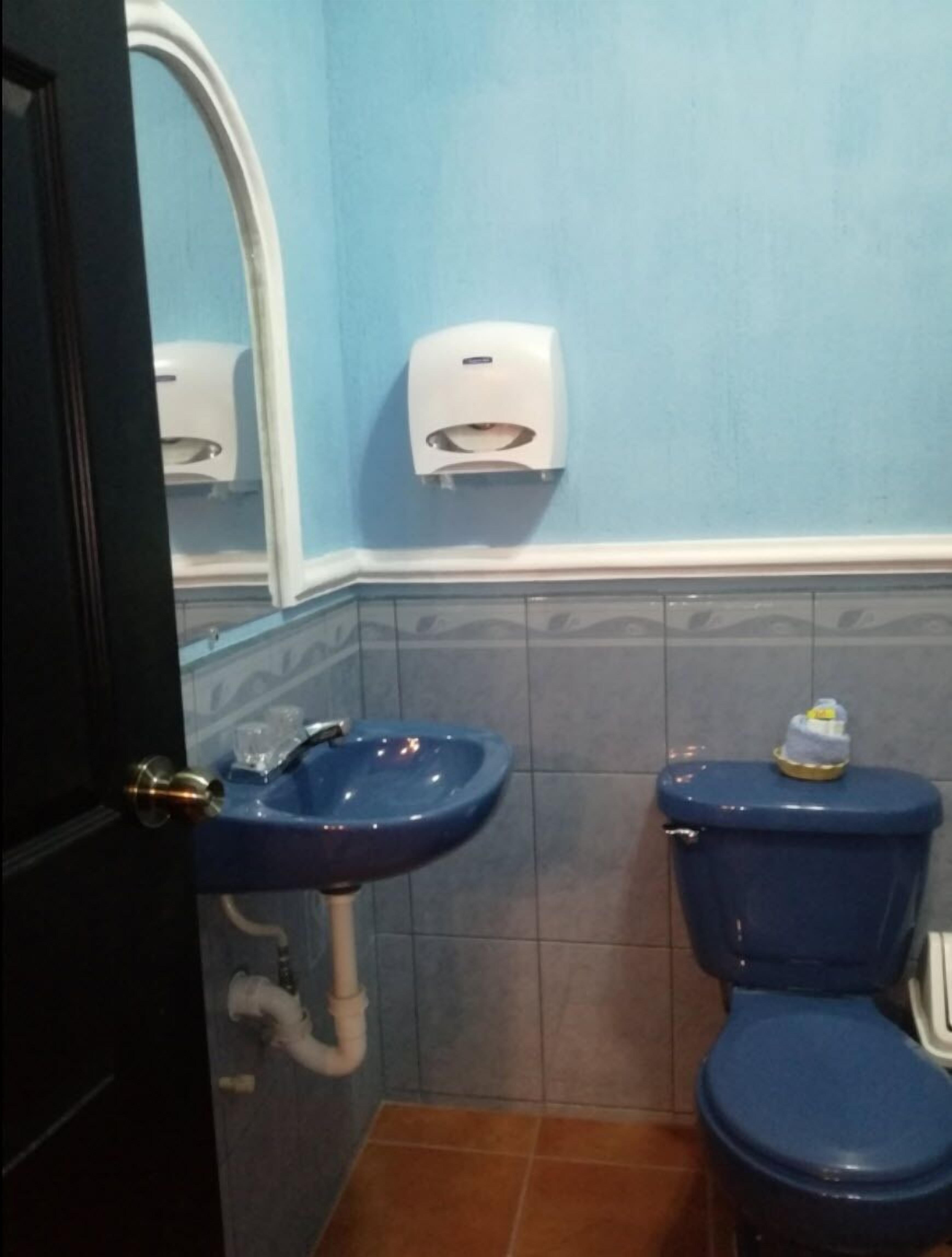 A bathroom with a blue sink, a toilet, and a hand dryer.
