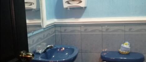 A bathroom with a blue sink, a toilet, and a hand dryer.